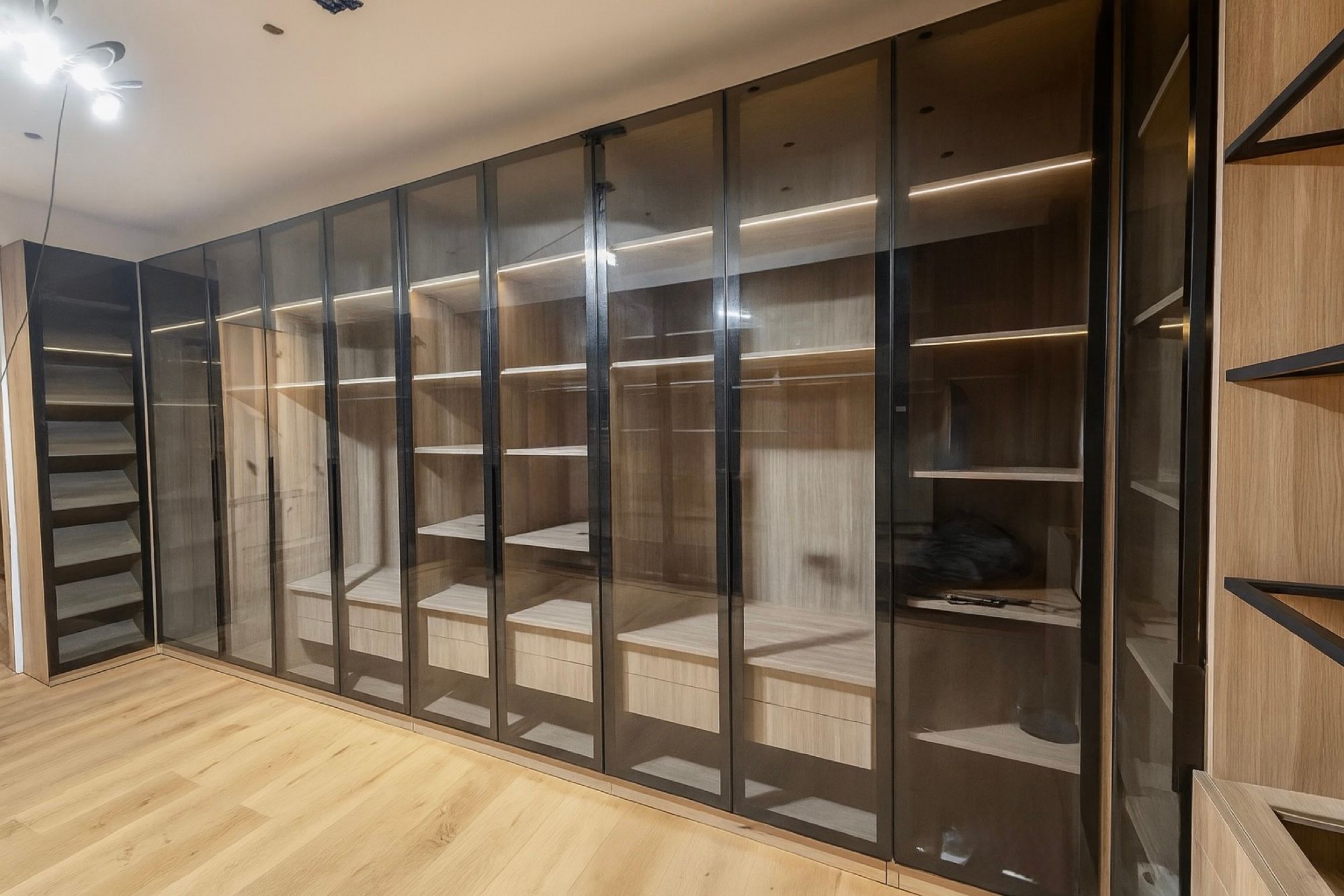 Wall of glass-front wardrobes with integrated shelf lighting