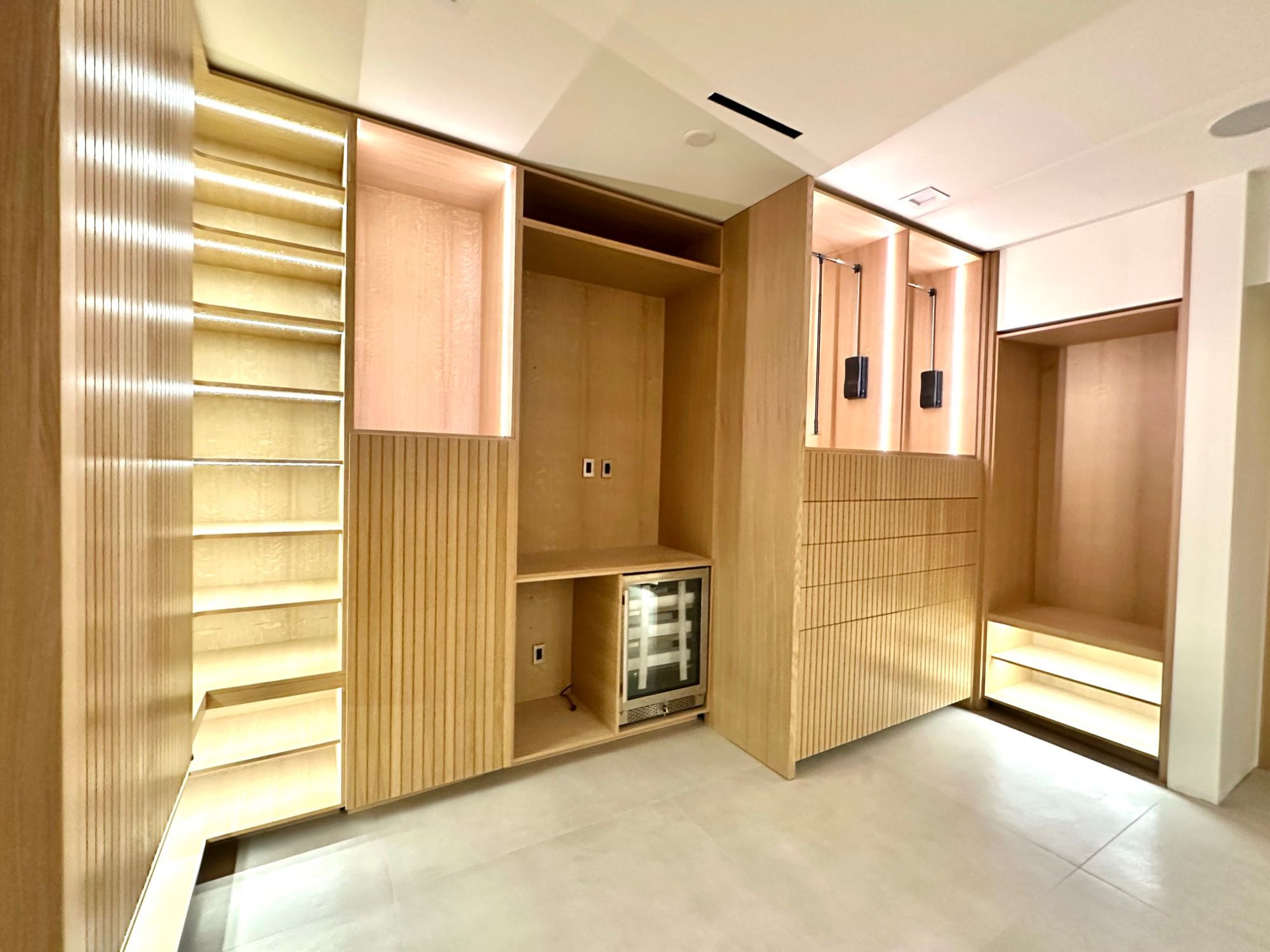 Dressing room corner with lit shelving, fluted oak and a built-in beverage fridge