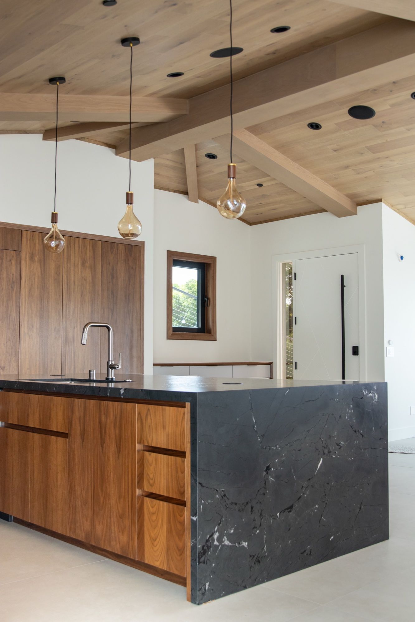 Walnut island with black marble waterfall under a beamed wood ceiling