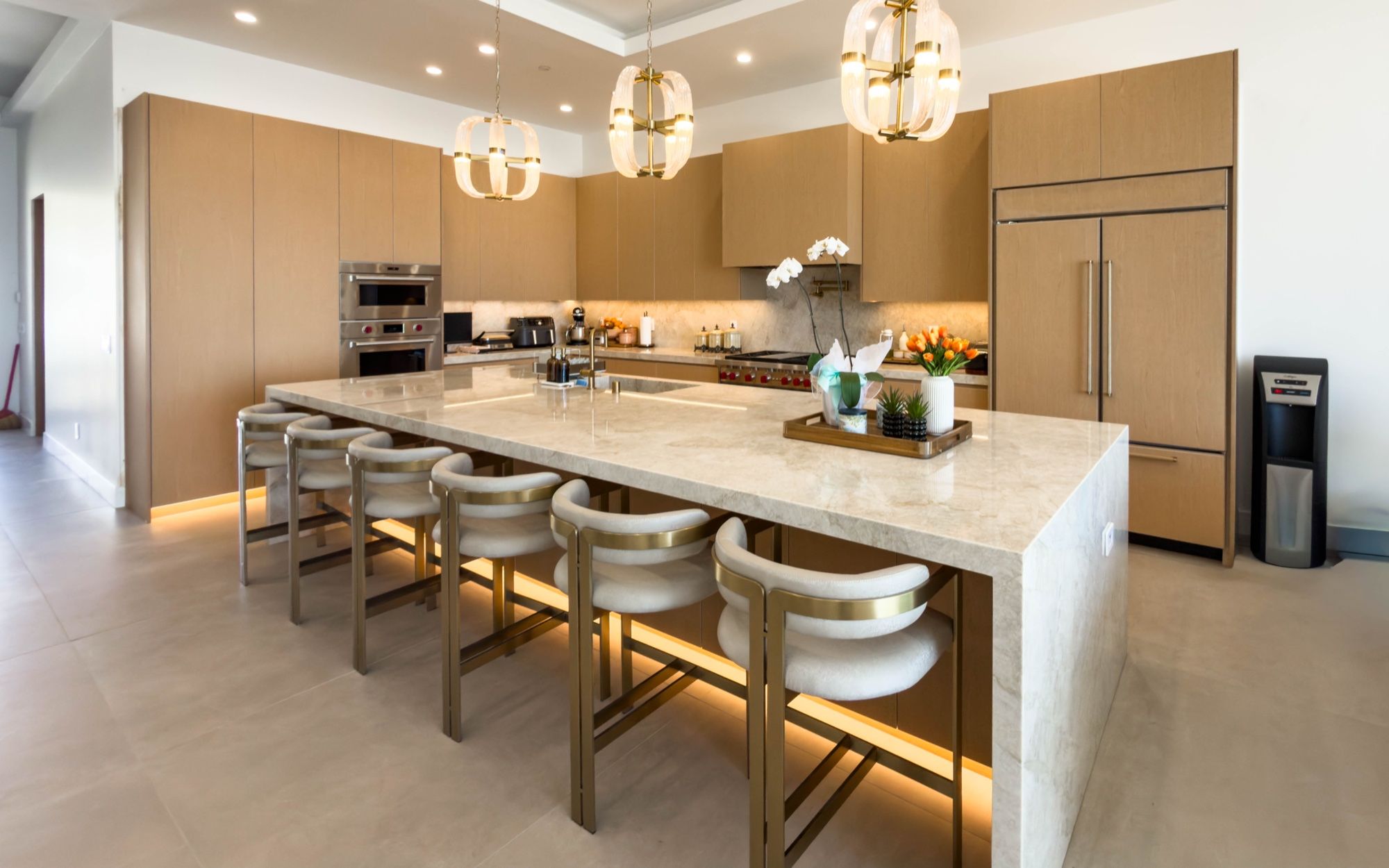 White oak kitchen with a long marble waterfall island, lit toe-kicks and pendant lights
