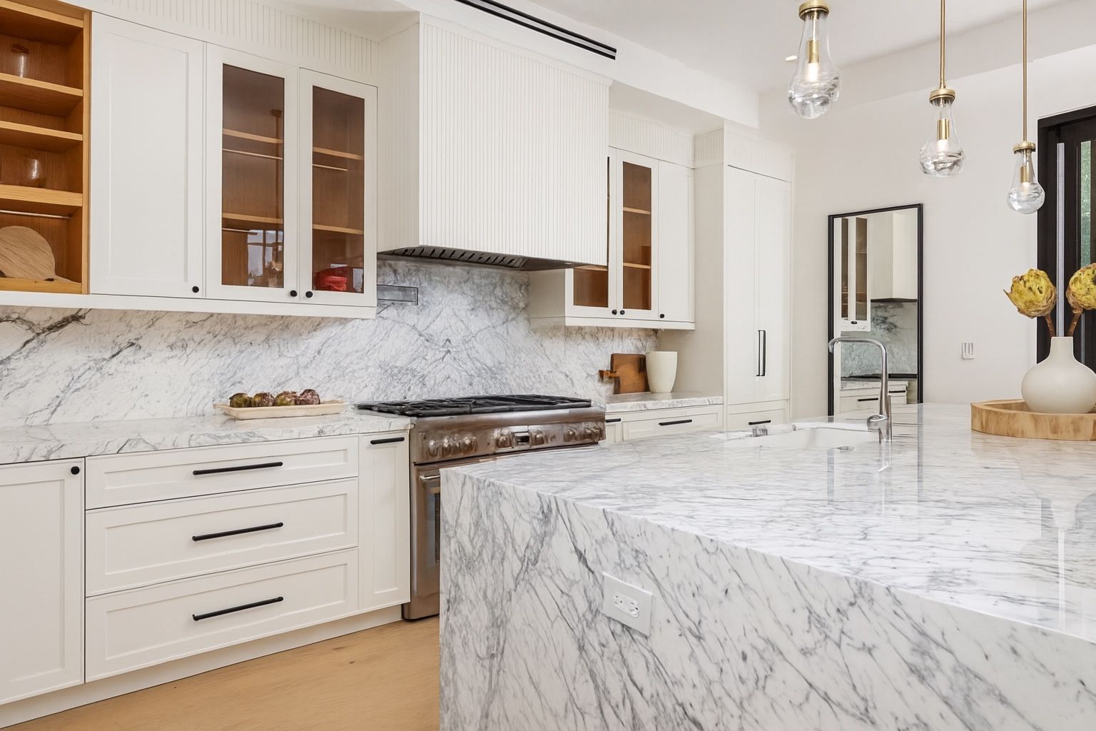 White shaker kitchen with glass uppers and a Calacatta marble waterfall island