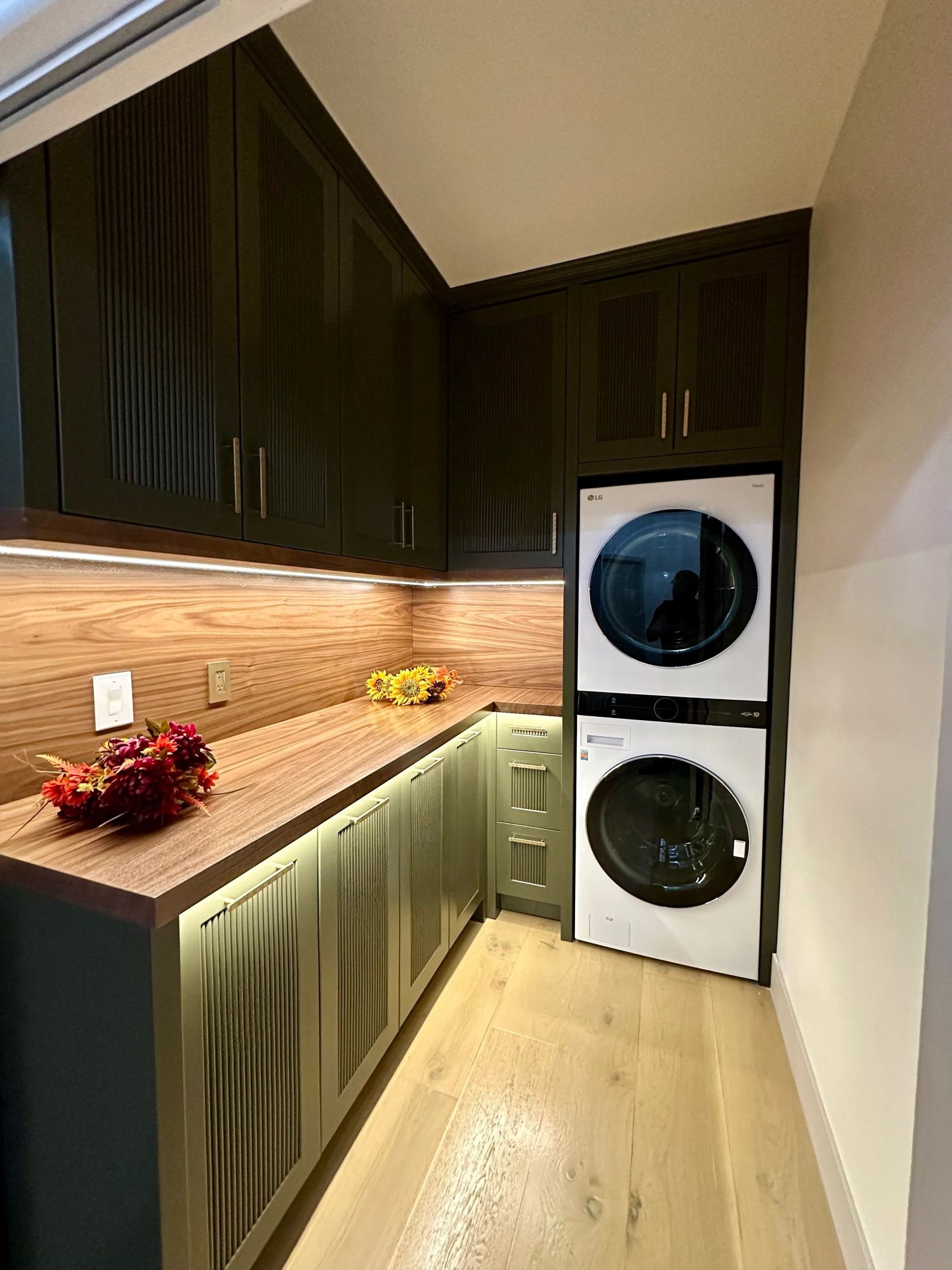Laundry room with dark green cabinets, butcher-block counter and stacked washer-dryer