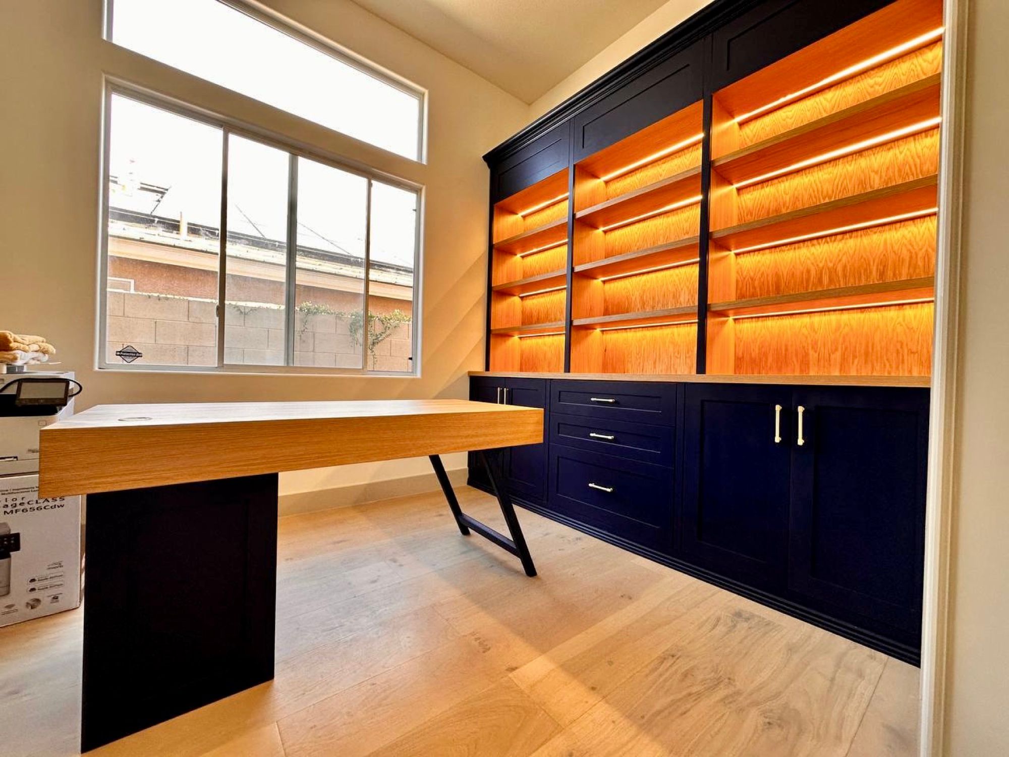 Home office with navy base cabinets, lit oak shelving and a floating desk